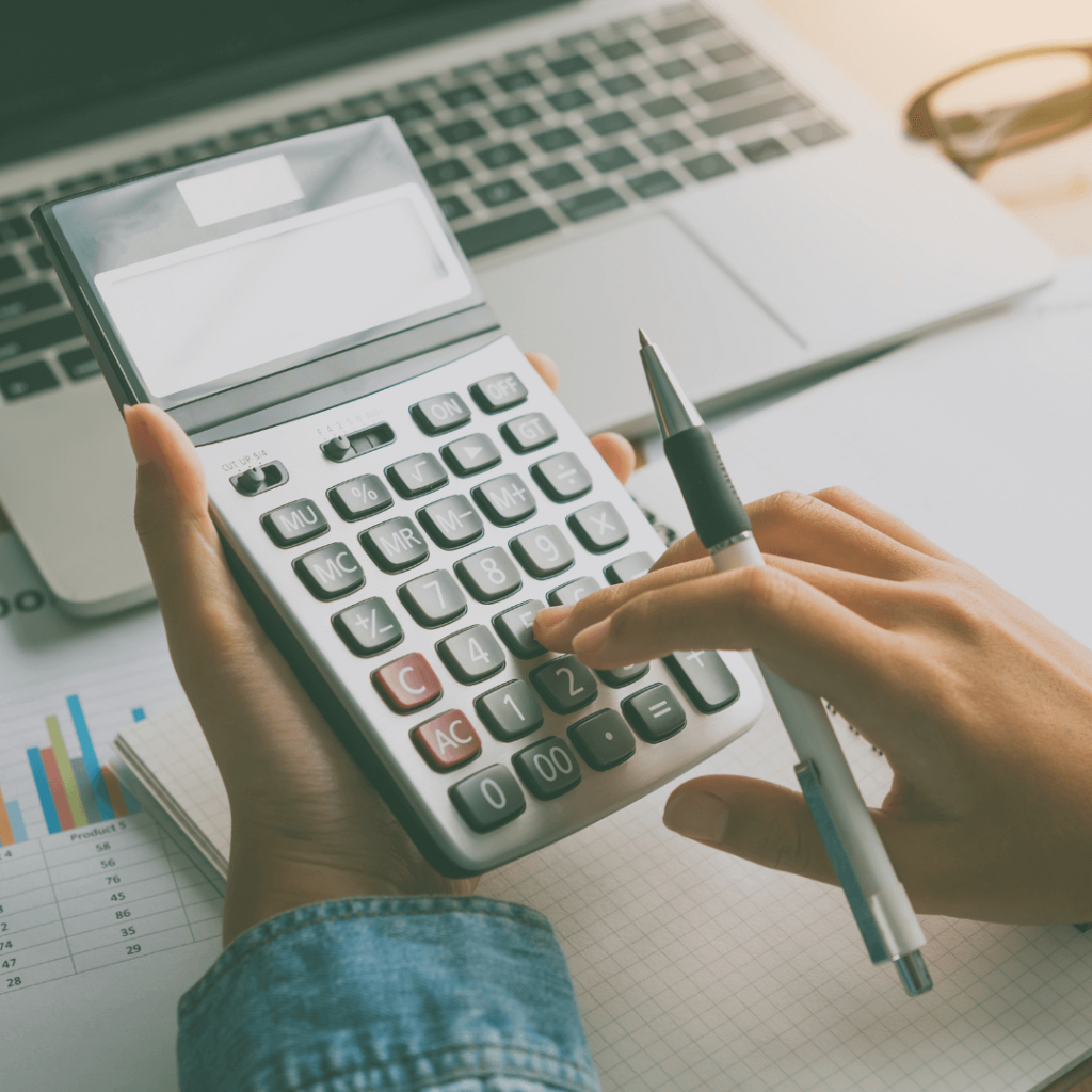 A woman typing on a calculator with a laptop in the background