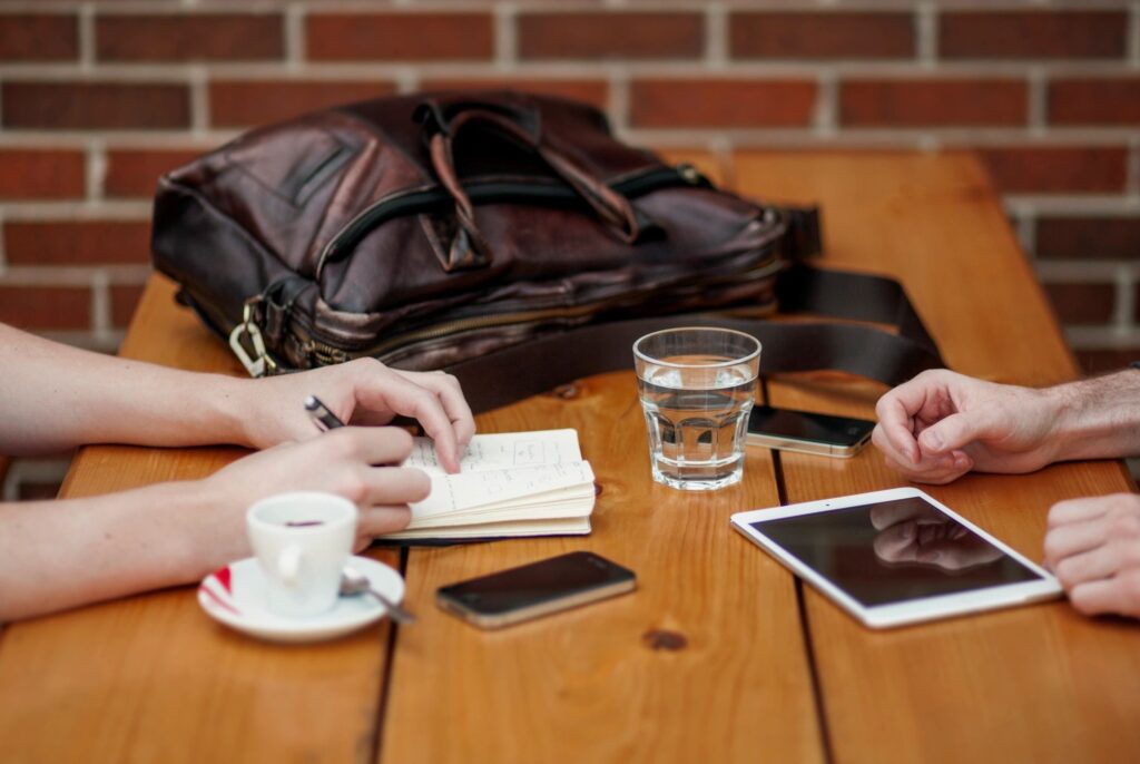 A picture of someone writing in a notebook while the person sitting across from them looks on.