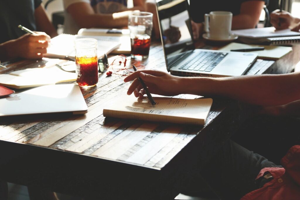 A picture of someone sitting at a desk writing in a notebook with pen.